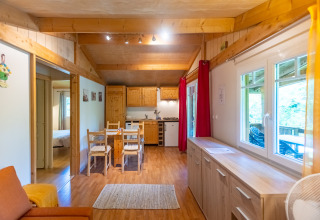 Cozy wooden interior of Chalet at Camping Des Randonneurs, France, with dining table and kitchen area.