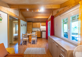 Cozy wooden interior of Chalet at Camping Des Randonneurs, France, with dining table and kitchen area.