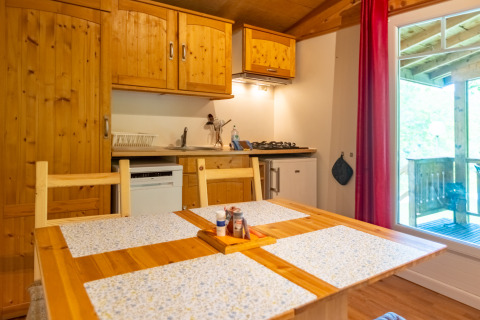 Interior view of the kitchen and dining table in the Chalet at Camping Des Randonneurs, France, with wood décor.
