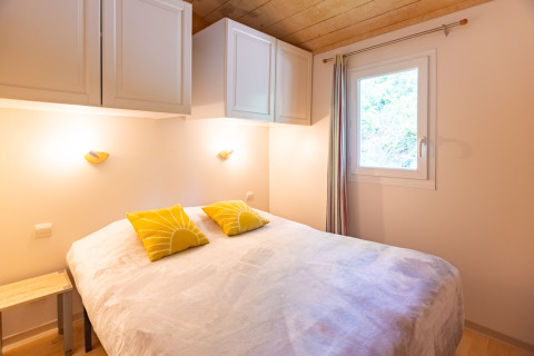 Bright bedroom in Chalet at Camping Des Randonneurs, France, featuring a double bed with yellow cushions.