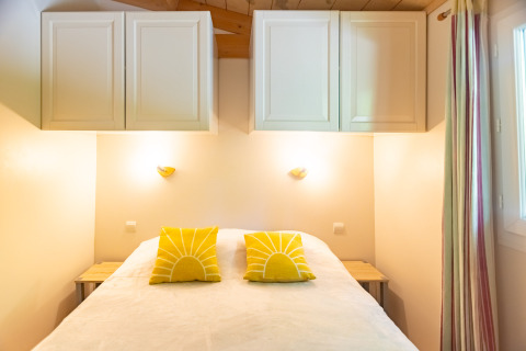 Bright bedroom in Chalet at Camping Des Randonneurs, France, with yellow pillows and overhead cabinets.