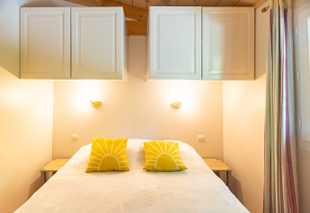 Camera luminosa nello Chalet al Camping Des Randonneurs in Francia con cuscini gialli e armadietti sopra il letto.