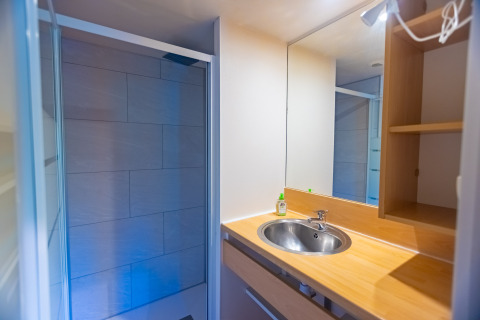 Modern bathroom with sink, mirror, and shower in a chalet at Camping Des Randonneurs in France.