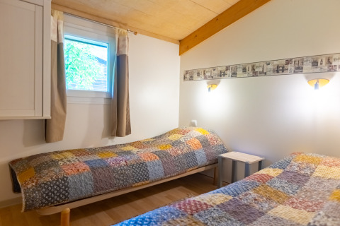Bedroom in Chalet at Camping Des Randonneurs, France, featuring two single beds with colorful patchwork quilts.