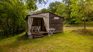 Tenda safari Stacaravan Tithome con facciata in legno, terrazza e sedie immersa in una zona verde.