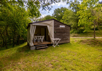 Safari-Zelt Stacaravan Tithome mit Holzverkleidung, Terrasse und Gartenmöbeln im grünen Waldgebiet.
