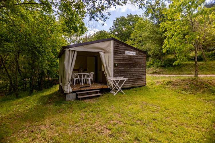 Tente safari Stacaravan Tithome avec façade boisée, terrasse et meubles de jardin, dans une zone verdoyante.