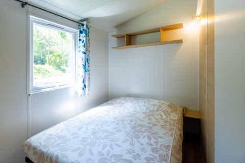 Helles Schlafzimmer im Stacaravan Tithome auf Camping Des Randonneurs in Frankreich mit Fenster und Bett.