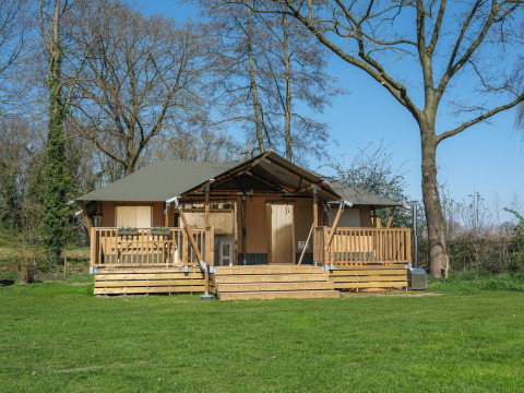 Safari-Zelt Medley Lodge mit Veranda, umgeben von grüner Wiese und Bäumen, ausgestattet mit Whirlpool.