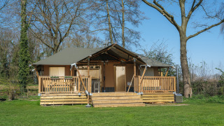 Medley Lodge safaritent met houten terras, bubbelbad en veel groen gras tussen grote bomen buiten.