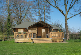 Medley Lodge safari tent with a hot tub, wooden deck, and surrounded by lush grass and tall trees outdoors.
