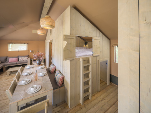 Interior of the Medley Lodge safari tent with dining table, kitchen, and loft bed at Den Blanken, Netherlands.