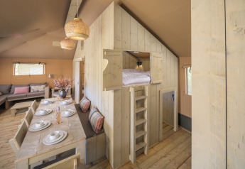 Interno della tenda safari Medley Lodge con tavolo da pranzo e letto rialzato a Den Blanken, Paesi Bassi.