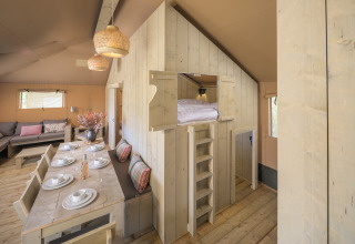 Interior de la tienda safari Medley Lodge con mesa de comedor y cama elevada en Den Blanken, Países Bajos.