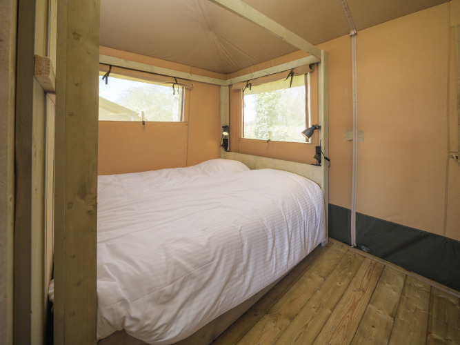 Habitación con cama doble en tienda safari Medley Lodge, parque Den Blanken, Países Bajos, interior cálido.
