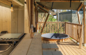 Buitenterras met houten zitbanken en bubbelbad bij Medley Lodge safaritent in Den Blanken recreatiepark.