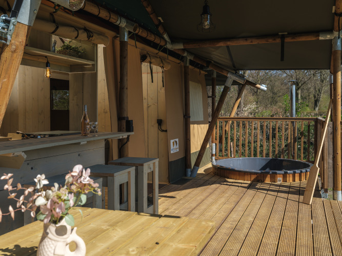 Terraza de madera con jacuzzi y zona de comedor en la tienda safari Medley Lodge en Den Blanken.