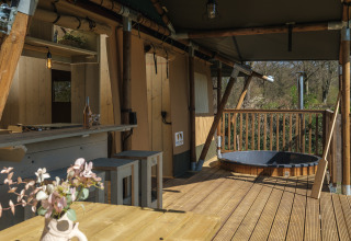 Terraza de madera con jacuzzi y zona de comedor en la tienda safari Medley Lodge en Den Blanken.