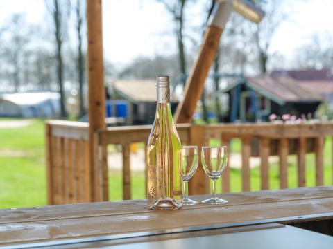 Botella de vino y dos copas sobre mesa de madera en tienda safari en Medley Lodge, Den Blanken, Países Bajos.