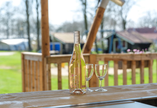 Botella de vino y dos copas sobre mesa de madera en tienda safari en Medley Lodge, Den Blanken, Países Bajos.