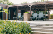 Area esterna di un lodge con terrazza in legno, sedie a sdraio, tavoli e fiori gialli in primo piano.