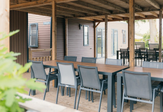 Udendørs spiseområde med borde og stole under overdækket terrasse ved Family lodge i De Boshoek, Holland.