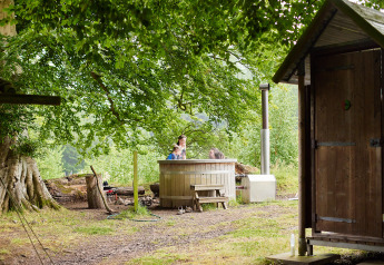 Safari tent with hot tub and private hot shower under trees at Feather Down Chesters, United Kingdom.