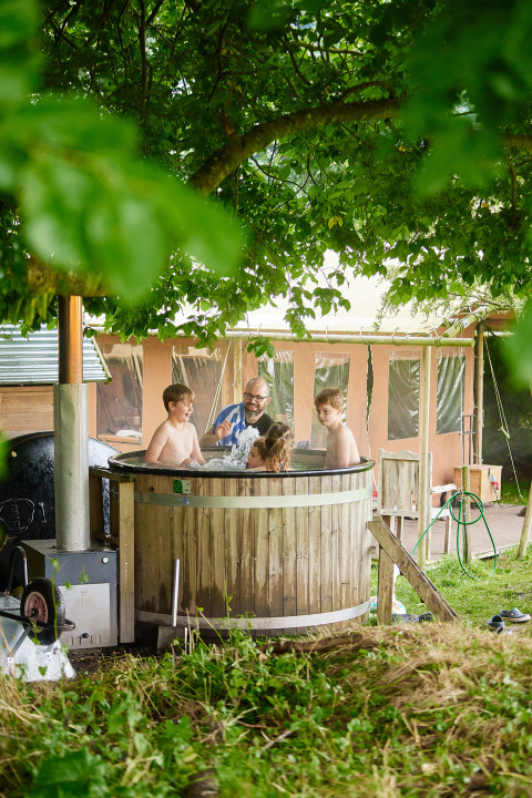 Gezin ontspant in een houten hot tub naast een safaritent bij Feather Down Chesters, Verenigd Koninkrijk.