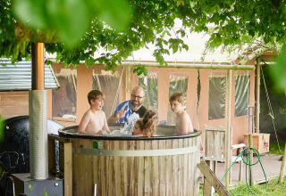 Gezin ontspant in een houten hot tub naast een safaritent bij Feather Down Chesters, Verenigd Koninkrijk.