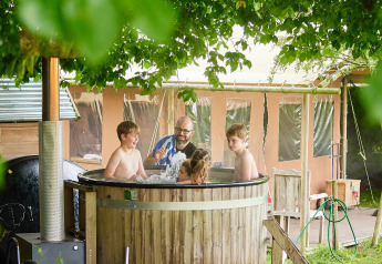 Family relaxing together in a wooden hot tub beside a safari tent at Feather Down Chesters, UK.