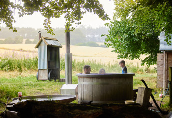 Family relaxing in a wood-fired hot tub and private shower beside safari tent at Feather Down Chesters, UK.
