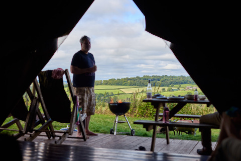 Blick aus einem Safarizelt auf Feather Down Billingsmoor Farm mit Mann, Grill und britischer Landschaft.