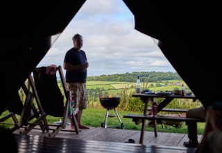 Blick aus einem Safarizelt auf Feather Down Billingsmoor Farm mit Mann, Grill und britischer Landschaft.