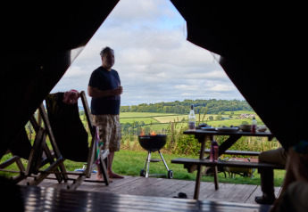 Vista desde la tienda safari en Feather Down Billingsmoor Farm con hombre, barbacoa y paisaje campestre.