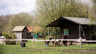 Safari tent named Tent Cottage with private hot shower and hot tub outside on a green grassy field by trees.