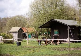 Safari-teltet Tent cottage med privat bruser og varmt kar set udefra på en grøn græsmark ved træer.
