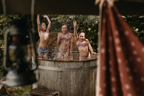 Des enfants s'amusent dans un bain chaud à côté d'une tente safari avec douche privée à Het Wesselink, Salland.