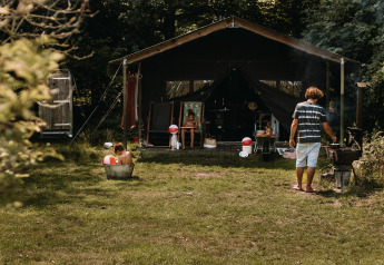 Familie nyder sommerdag foran safaritelthytte med udendørs bad og boblebad i Nederlandene.