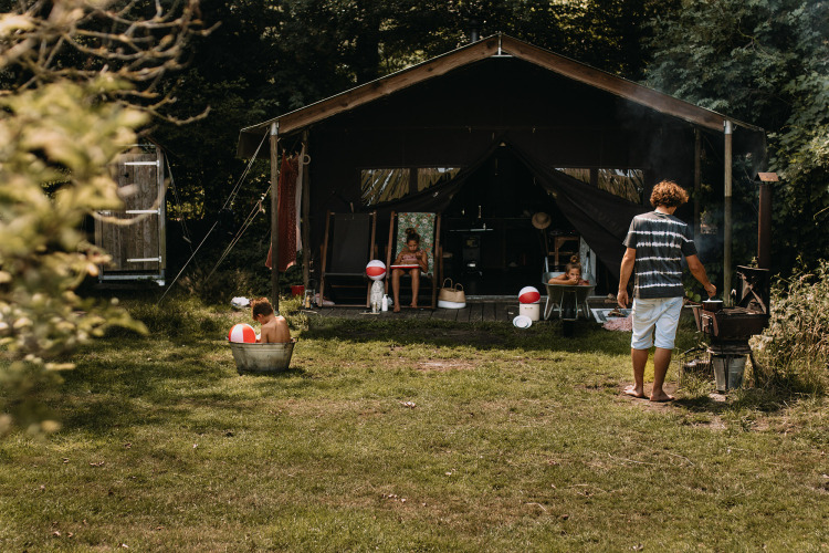 Familia disfruta afuera de una tienda safari con ducha privada y jacuzzi en los Países Bajos.