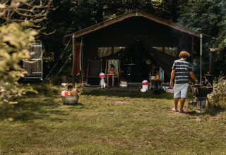 Familia disfruta afuera de una tienda safari con ducha privada y jacuzzi en los Países Bajos.