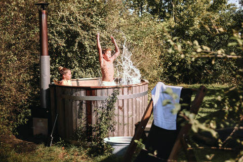 Zwei Kinder spielen in einem Outdoor-Whirlpool bei ihrem Safarizelt, umgeben von üppigem Grün.