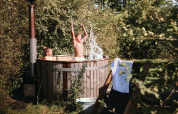 Zwei Kinder spielen in einem Outdoor-Whirlpool bei ihrem Safarizelt, umgeben von üppigem Grün.