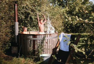 Dos niños se divierten en una bañera de madera al aire libre cerca de su tienda safari, rodeados de naturaleza.