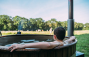 Persoon ontspant in een houten hottub bij de safaritent van Feather Down Landgoed Volenbeek in een groene wei.