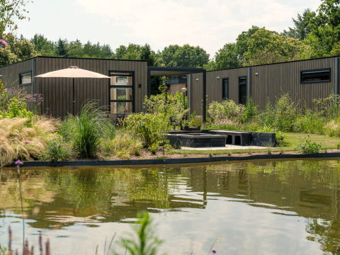 Batenburgh Deluxe lodge at Veluwepark de Bosgraaf in the Netherlands, modern exterior, pond, and lush garden.