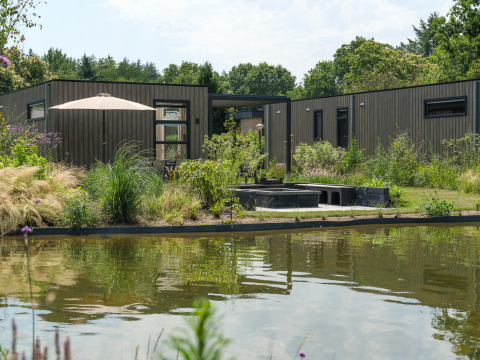 Batenburgh Deluxe lodge at Veluwepark de Bosgraaf in the Netherlands, modern exterior, pond, and lush garden.