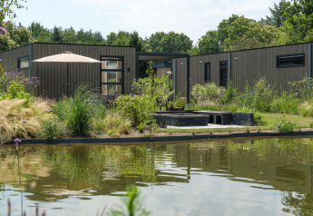 Batenburgh Deluxe lodge at Veluwepark de Bosgraaf in the Netherlands, modern exterior, pond, and lush garden.