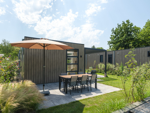 Terrazza esterna con ombrellone e tavolo presso il lodge Batenburgh Deluxe a Veluwepark de Bosgraaf, Paesi Bassi.