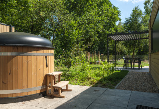 Udendørs område med en træboblebad, lille trappe, siddeplads og grønne træer ved Loevestein Comfort Lodge.