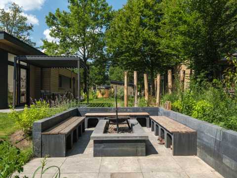 Udendørs opholdsområde med bænke og bålplads ved Loevestein Deluxe-lodge på Veluwepark de Bosgraaf i Holland.